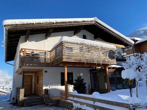 Ein zweistöckiges Chalet mit Balkon, Holzbalken und einem mit Schnee bedeckten Dach.