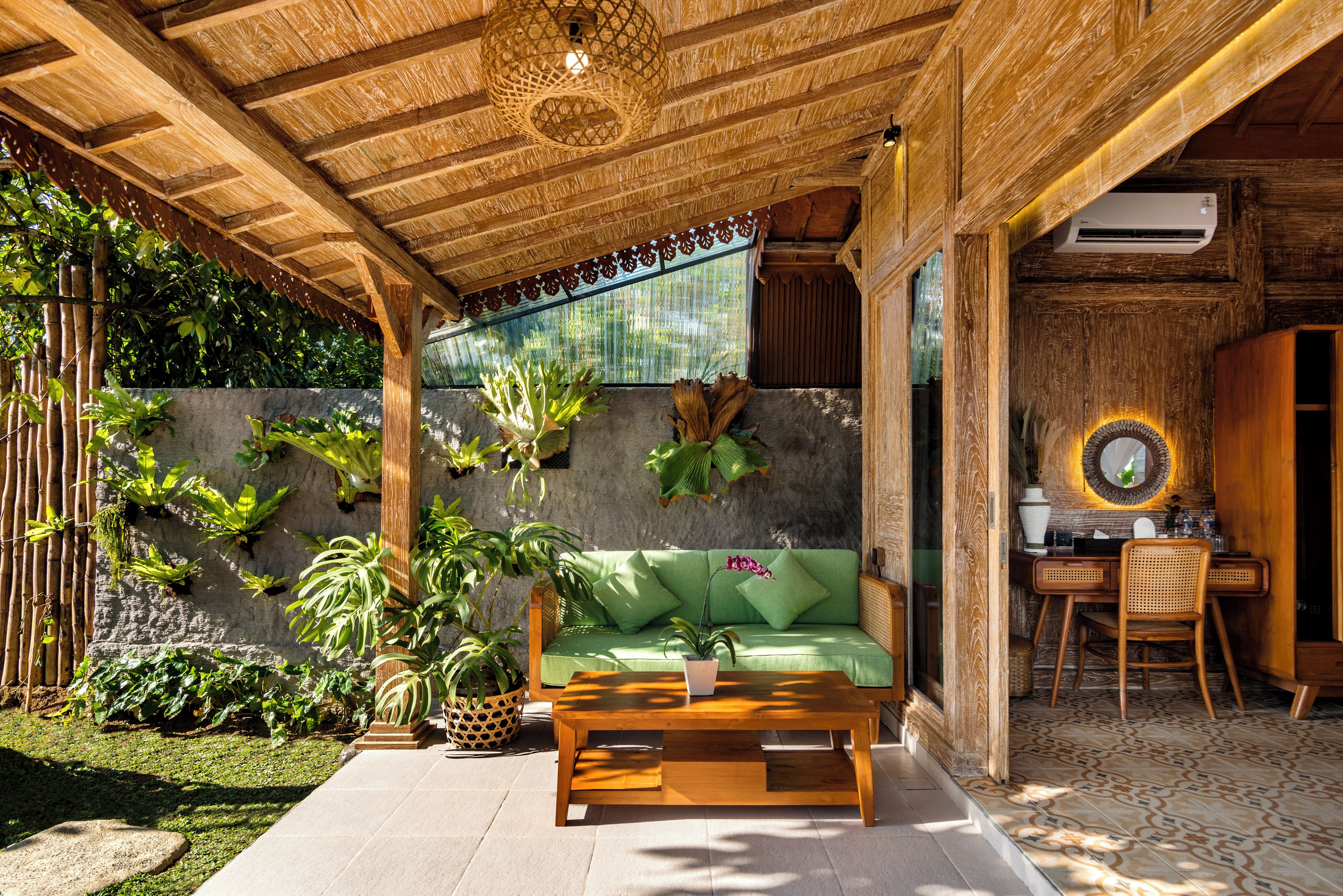 Eine Holzbalkendecke mit einer gewebten Leuchte, ein grünes Sofa mit Kissen, ein Holztisch und ein Topfpflanze.