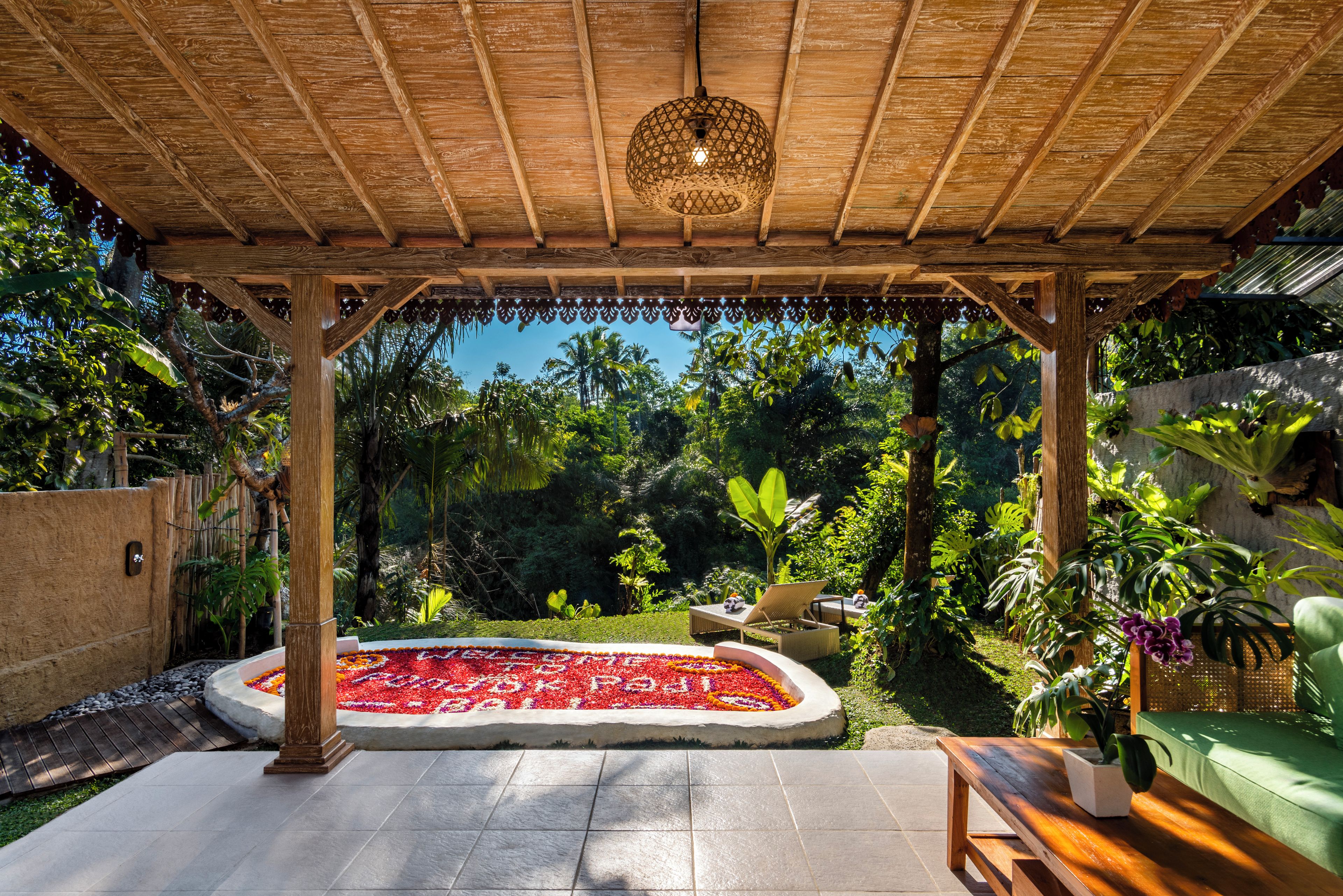 A covered patio area with a wooden ceiling, a decorative light fixture, and a flower bed with red and white flowers.