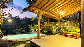 A covered outdoor area with a pool, seating, and lush greenery.