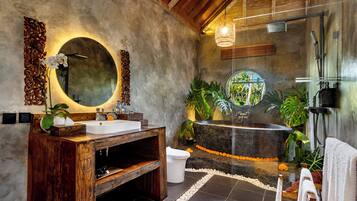 Une salle de bain avec un meuble-lavabo en bois, un miroir rond, une baignoire sur pieds et un espace douche.