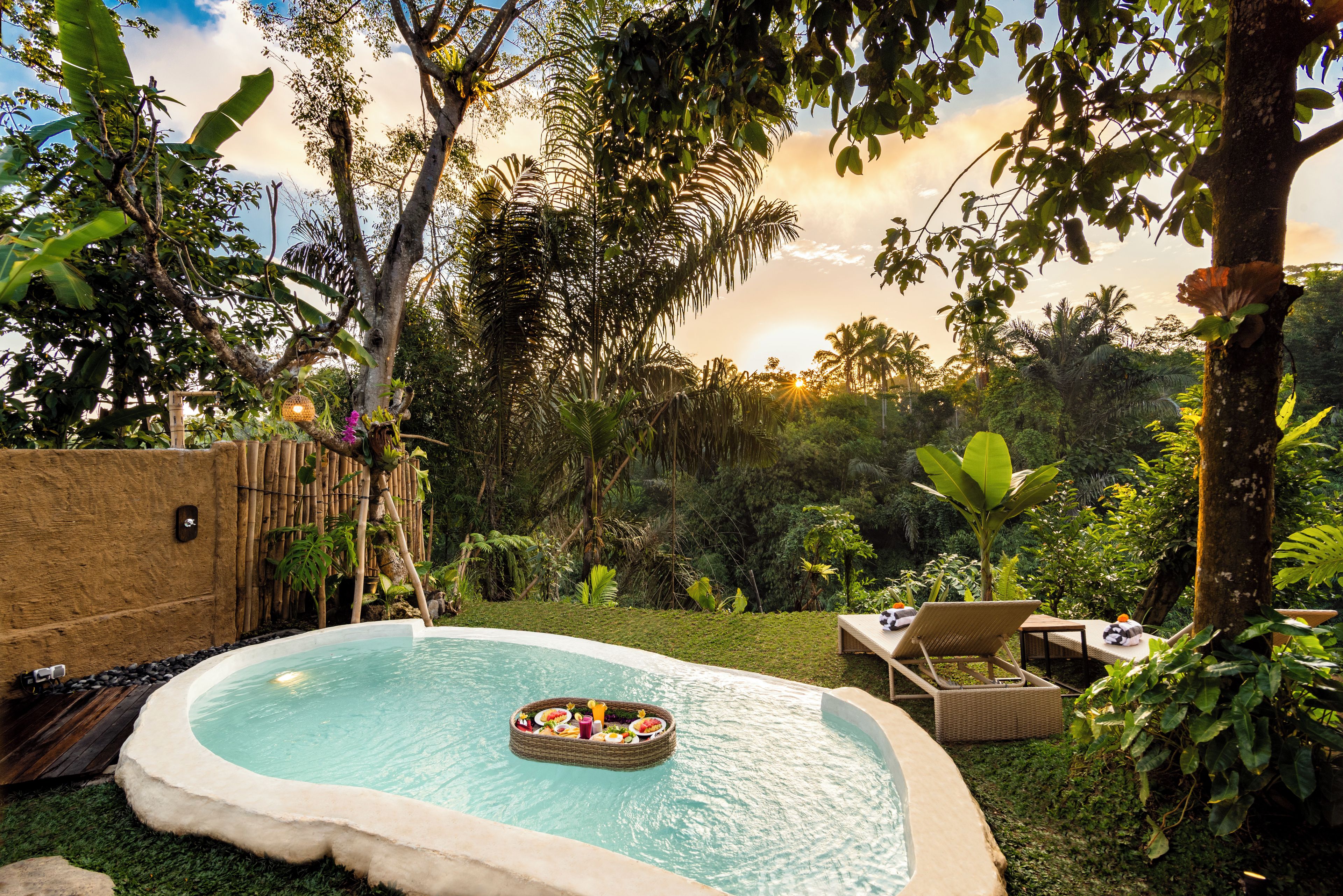A pool with a floating bar, surrounded by lush greenery and a bamboo fence.