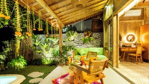 Un espacio al aire libre acogedor con un sofá verde, sillas de madera y una mesa lista para comer.