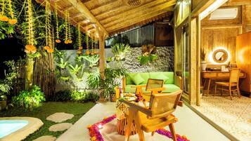 Un espacio al aire libre acogedor con un sofá verde, sillas de madera y una mesa lista para comer.