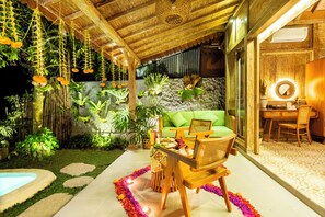 Un espacio al aire libre acogedor con un sofá verde, sillas de madera y una mesa lista para comer.
