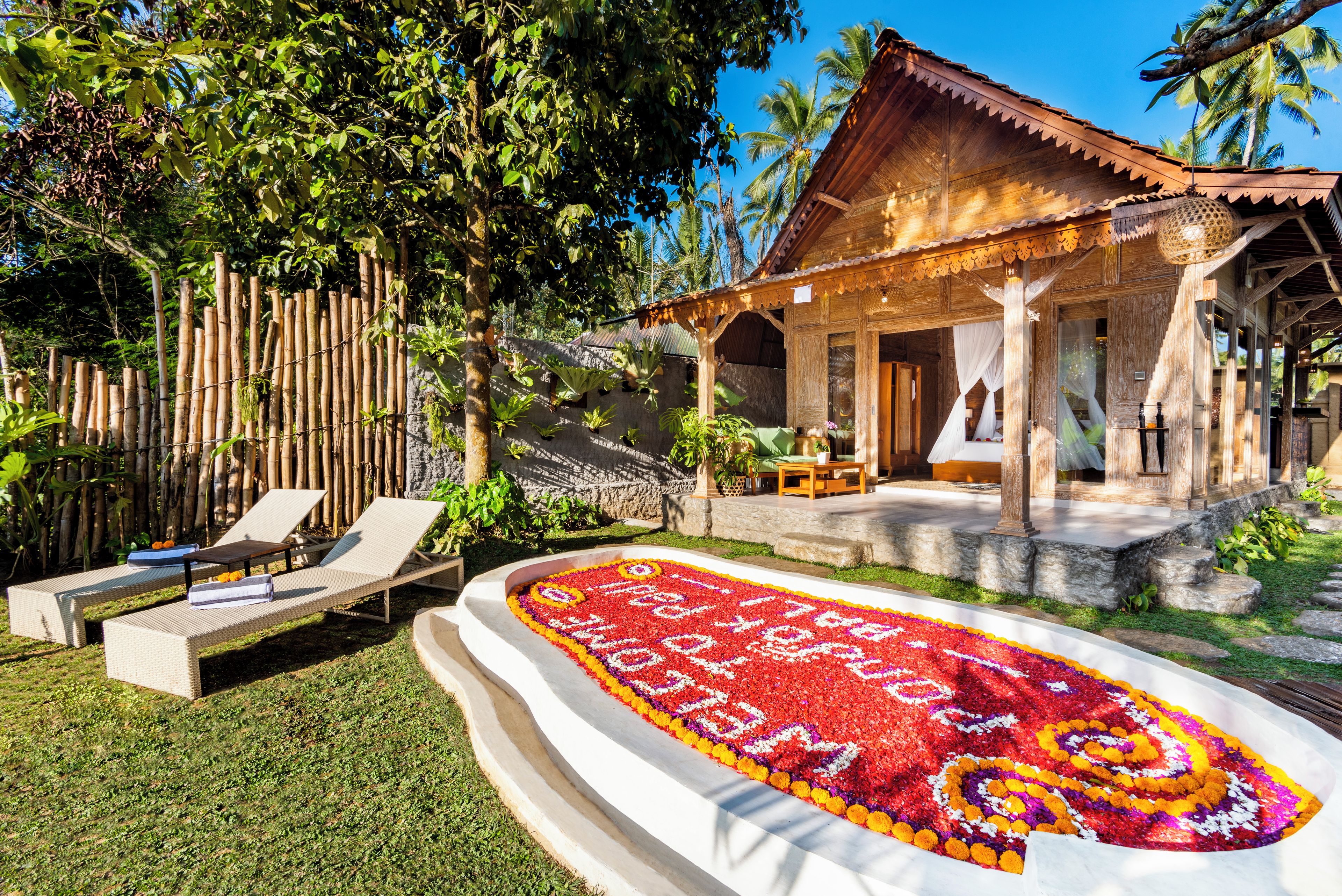 A wooden villa with a covered porch, a flower-decorated lawn, and a bamboo fence.