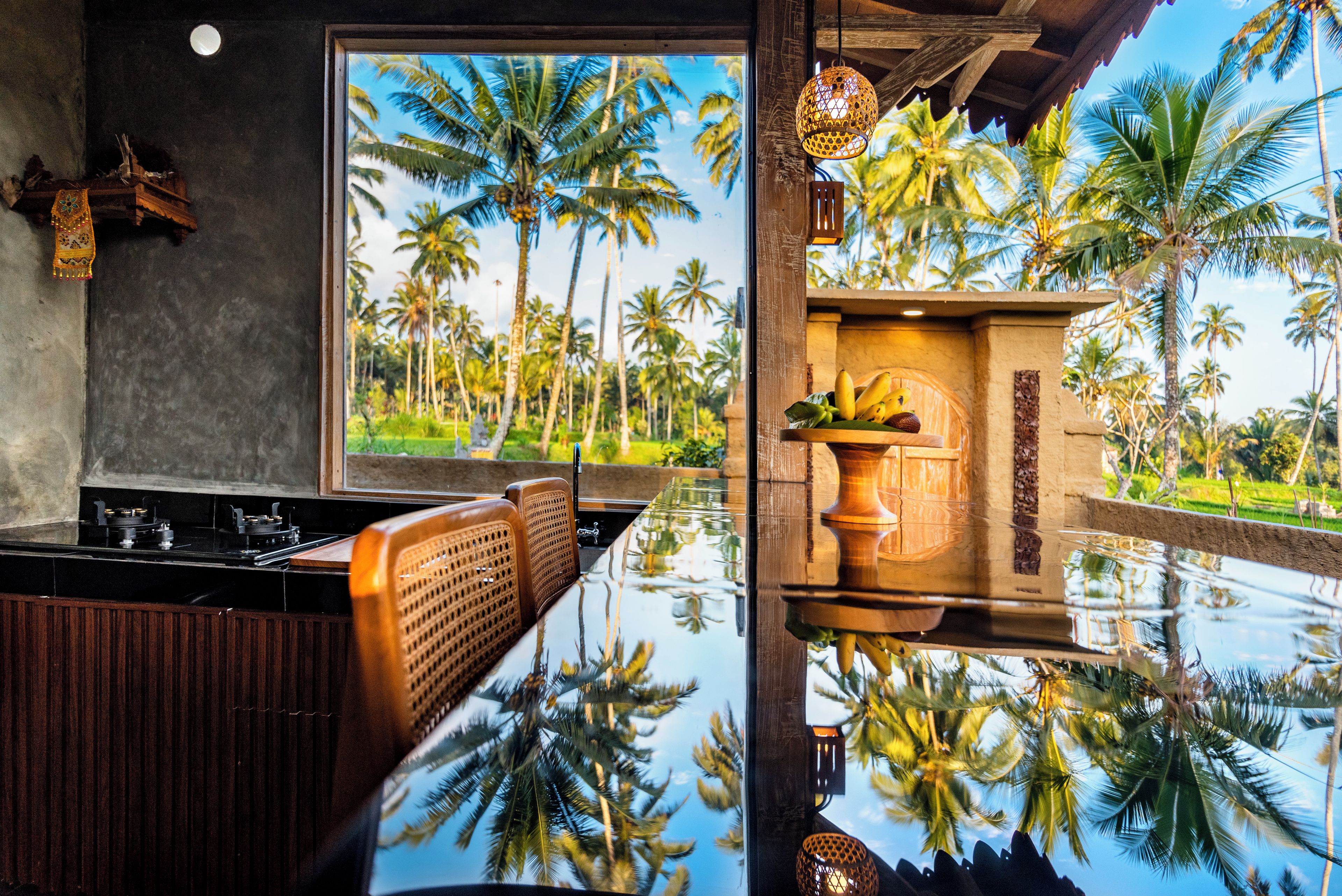 A modern kitchen with a large window, wooden furniture, and a view of palm trees.