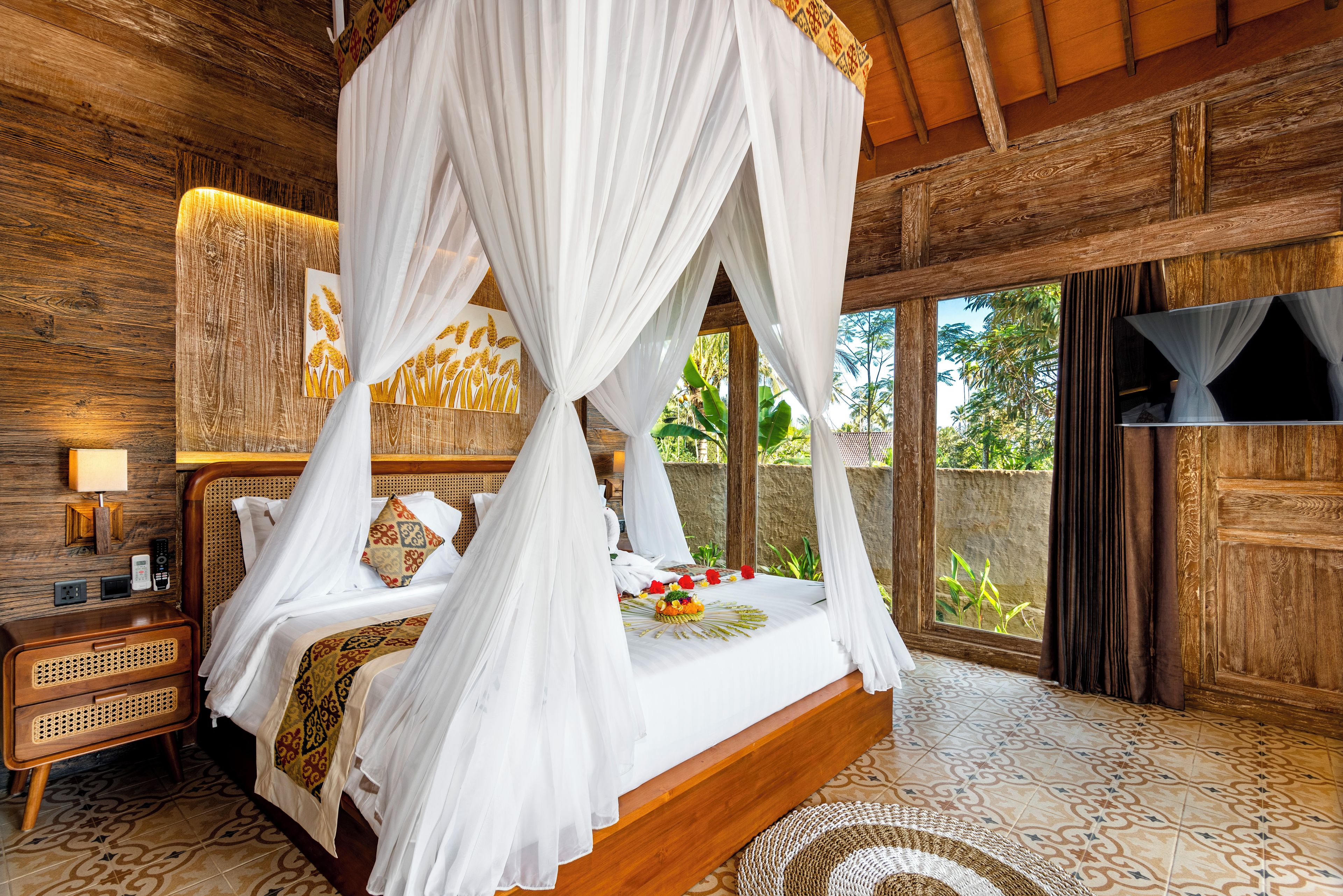A four-poster bed with white drapes, a wooden headboard, and a woven rattan nightstand with a lamp.