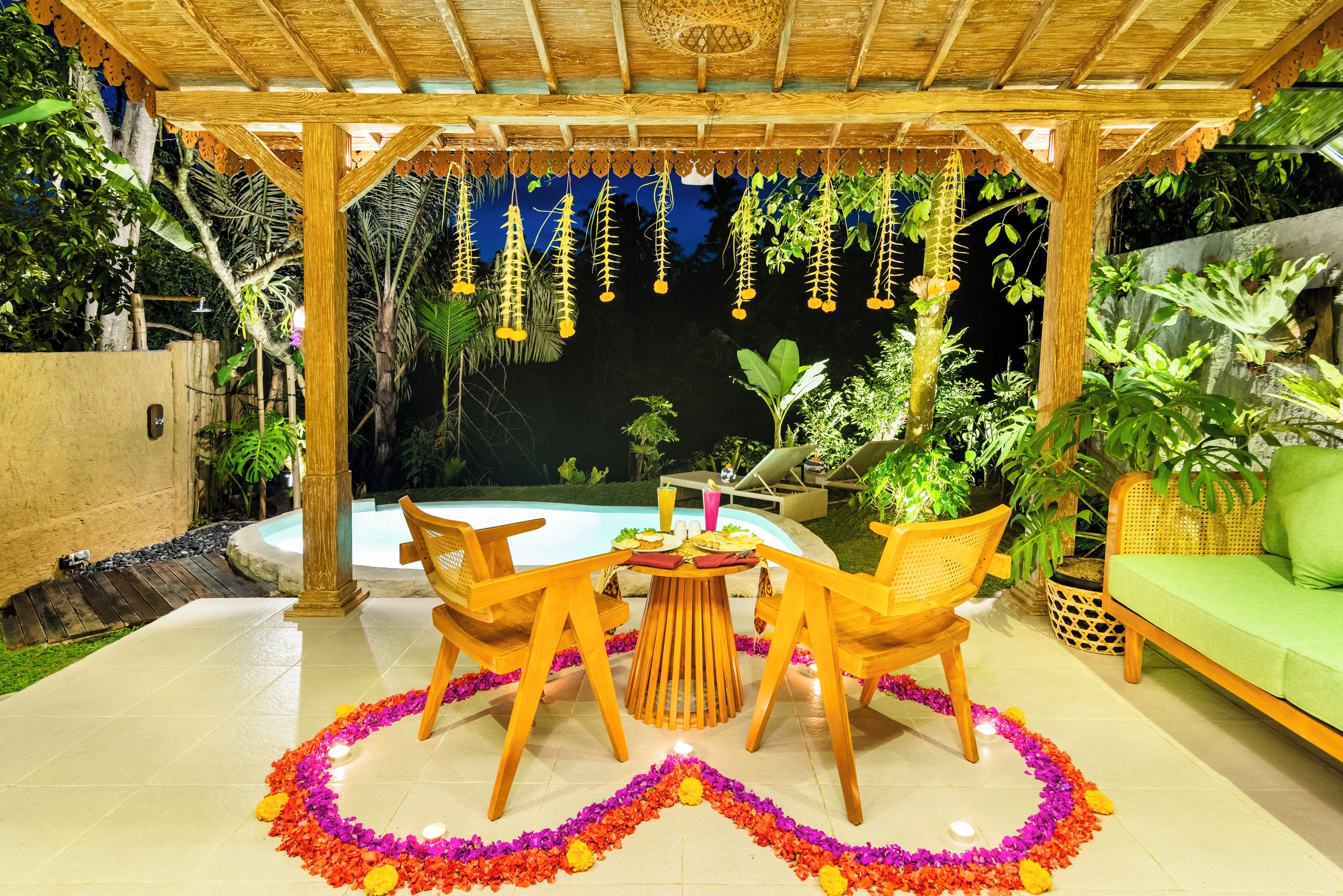 Un patio exterior con piscina, rodeado de exuberante vegetación y una pérgola de madera.