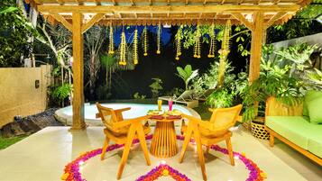 Un patio exterior con piscina, rodeado de exuberante vegetación y una pérgola de madera.