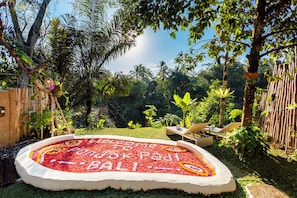 Un jardín con un parterre circular, una valla de bambú y sillones de descanso.