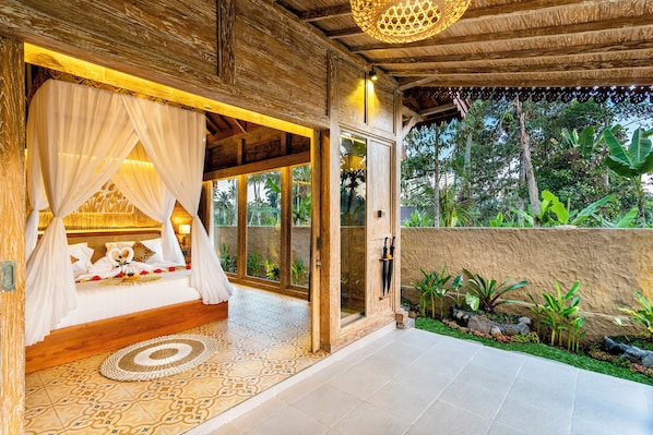 A room with a bed, a canopy, and a view of the garden. - Pondok Padi Bali Villa (Taro)