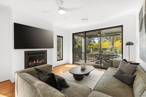 Un salon moderne doté d’une cheminée, d’un téléviseur à écran plat, d’un ventilateur de plafond et d’une grande porte-fenêtre coulissante donnant sur un patio extérieur.