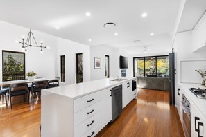 A modern kitchen with a central island, built-in appliances, and a dining area with a view. - KARINYA LODGE - The Vintage Holiday Houses (POKOLBIN)