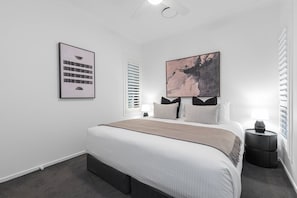 A modern bedroom with a large bed, a nightstand, a wall-mounted lamp, and two framed artworks. - KARINYA LODGE - The Vintage Holiday Houses (POKOLBIN)