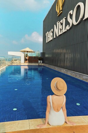 Eine Person sitzt am Pool, im Hintergrund ein großes Gebäude mit der Aufschrift 'THE NELSON'.