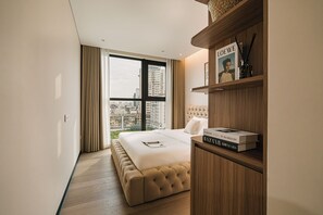 Ein Hotelzimmer mit einem großen Bett, einem Holzkopfende, einem Bücherregal mit Büchern und Blick auf die Stadt durch das Fenster.