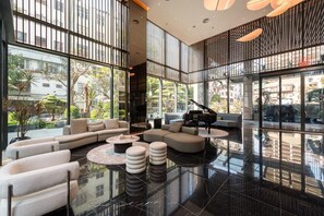 A spacious living area with a grand piano, modern furniture, and large windows offering a view of the cityscape. - The Nelson Luxury Apartment 3Bedroom - FREE Pool, Gym & Sauna (Hà Nội)