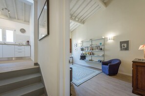 A staircase leading to a kitchen with white cabinets, a dining area with a blue chair, and a bookshelf with various items. - Apartments Florence - Mona Lisa Charme (Firenze)