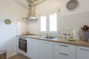 Eine Küche mit weißen Schränken, einer Edelstahl-Spüle, einem Gasherd und einem Fenster über der Spüle.