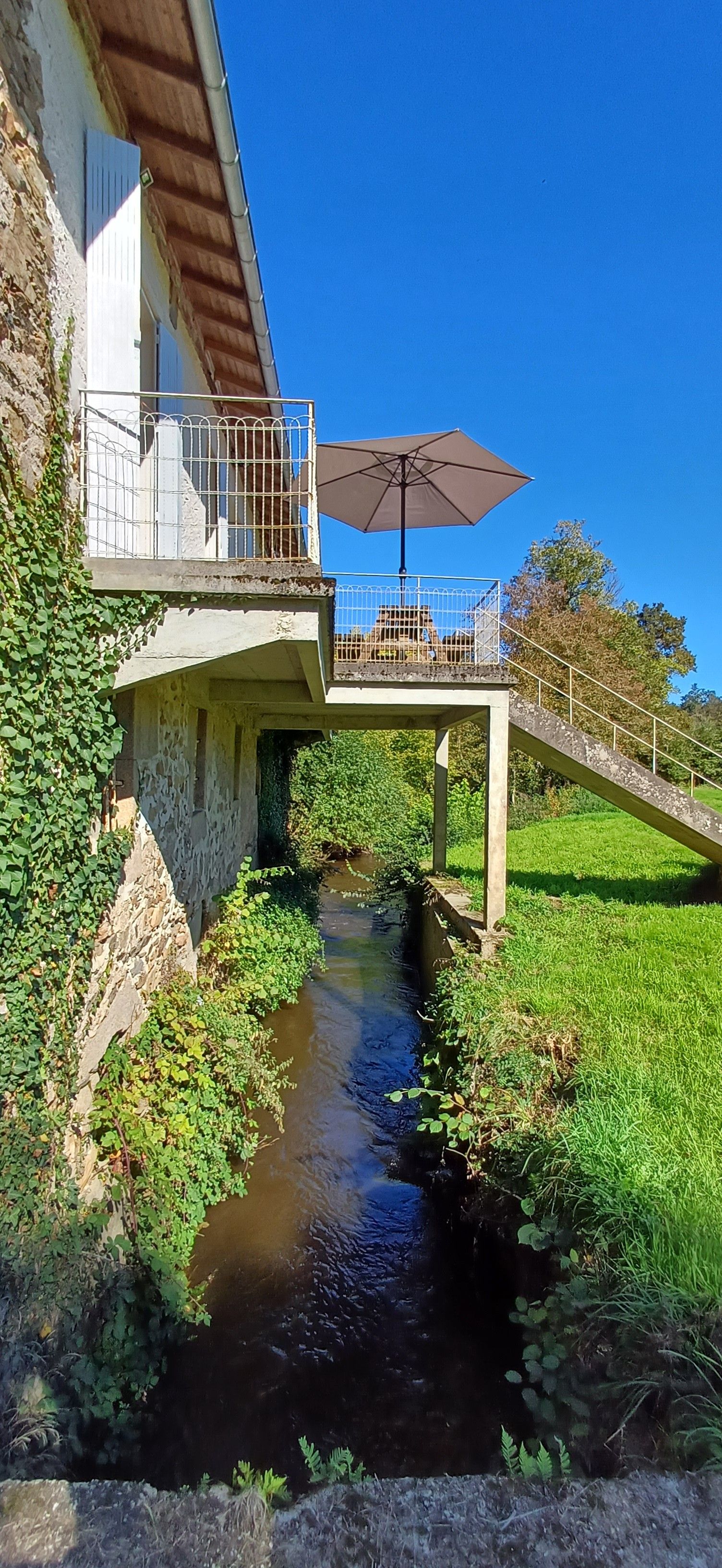 A house with a balcony overlooking a narrow stream.
