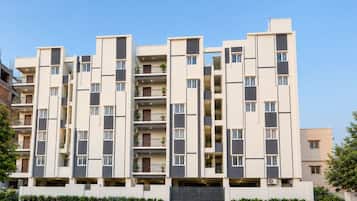 A multi-story residential building with balconies, a gated entrance, and a clear sky.