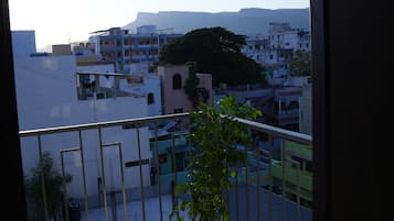 A balcony with a potted plant, a view of a cityscape with buildings, and a clear sky.