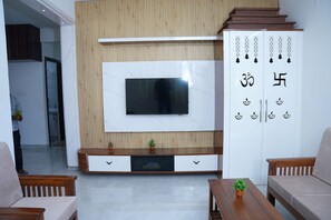 Una sala de estar moderna con un televisor de pantalla plana montado en una pared de madera, un sofá, una mesa de centro y un mueble con símbolos decorativos.