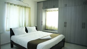 A bedroom with a bed, a window with curtains, and a wardrobe.