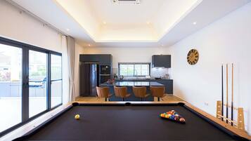 A modern kitchen with a central island, a pool table, and a dining area with chairs.