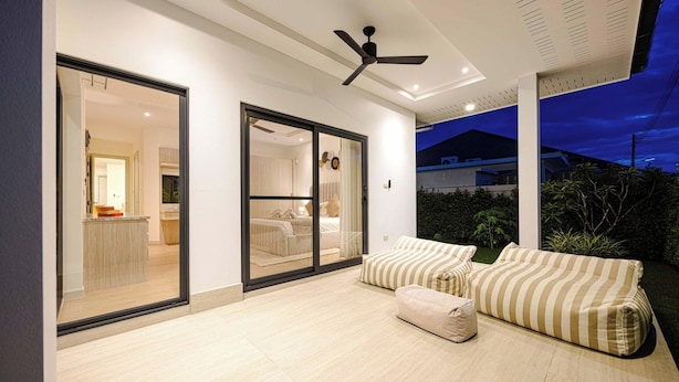 A modern bedroom with a large sliding glass door leading to a bathroom, a ceiling fan, and a view of the outside. - Modern 3BR Villa w/ Private Pool (MV55) (Hua Hin)