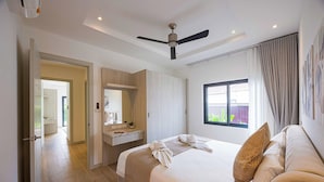A hotel room with a bed, a vanity with a mirror, a ceiling fan, and a window with a view of greenery. - Modern 3BR Villa w/ Private Pool (MV55) (Hua Hin)