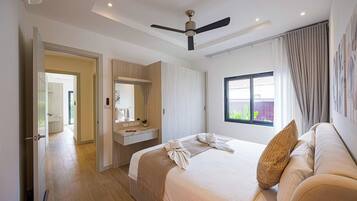 Une chambre d’hôtel avec un lit, une coiffeuse avec un miroir, un ventilateur de plafond et une fenêtre donnant sur un paysage verdoyant.