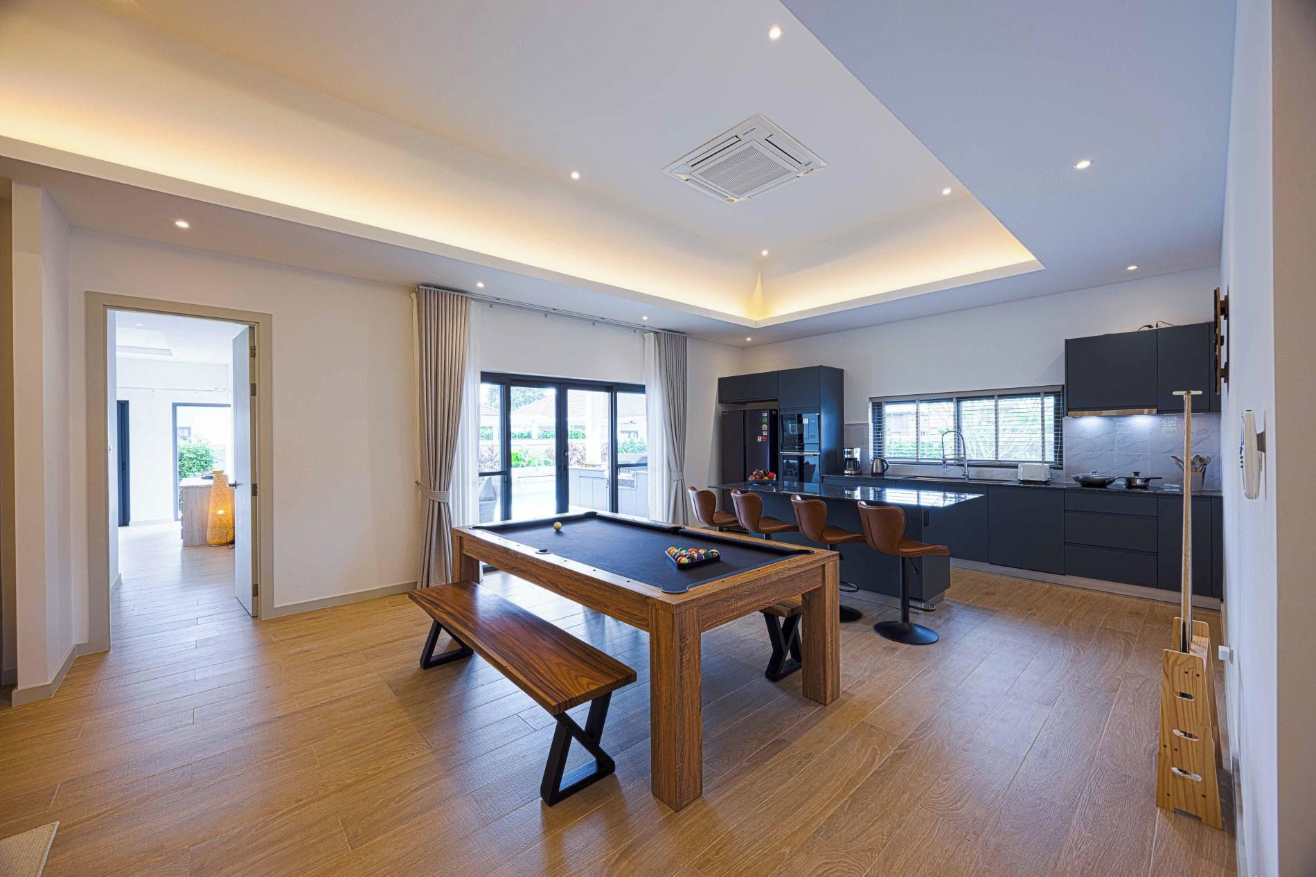 A modern living room with a pool table, a dining area, and a kitchen.
