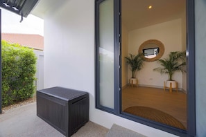 Una entrada moderna con puerta corredera de vidrio, un pequeño espacio de estar al aire libre y un espejo fijado a la pared.