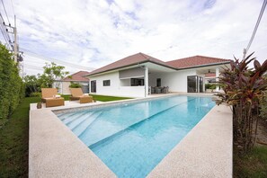 Una casa moderna con piscina, mobiliario exterior y un área de patio techada.