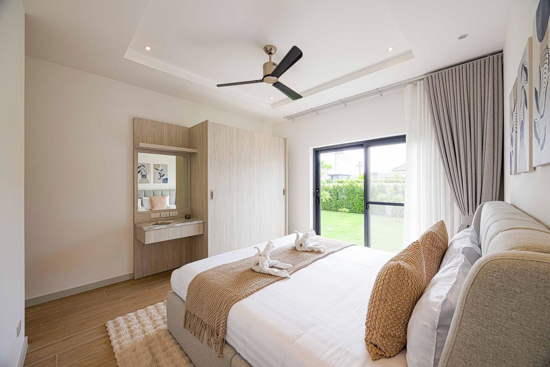 Un dormitorio con cama, ventilador de techo, ventana grande con cortinas y vistas al exterior.