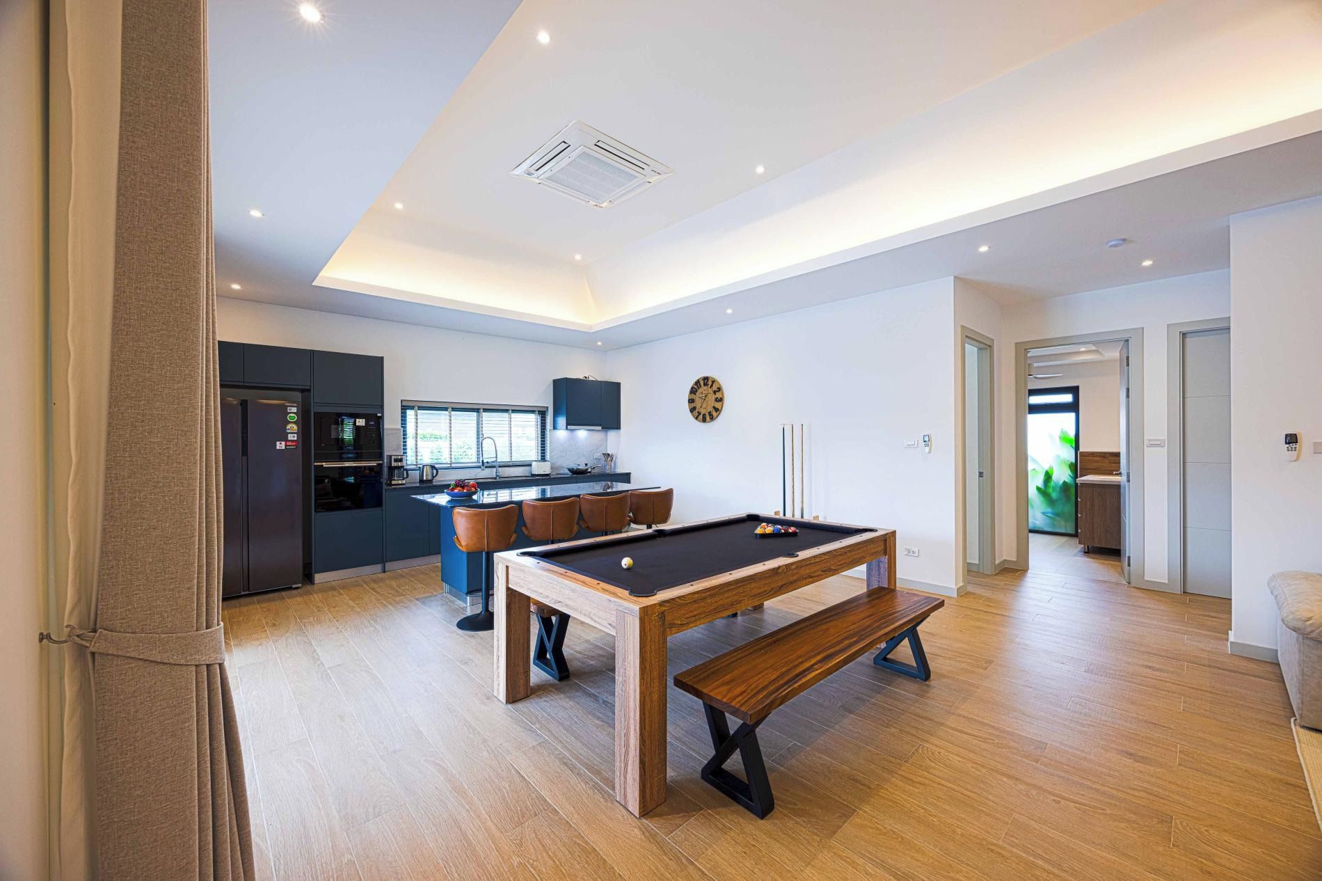 Una cocina moderna con horno empotrado, un comedor con mesa de billar y una sala de estar con sofá y puerta a otra habitación.