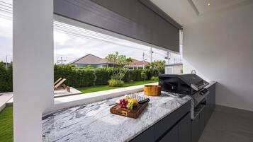 A modern kitchen with a marble countertop, a built-in grill, and a view of a residential area.