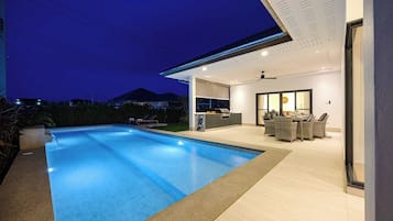 Un espace piscine extérieur moderne, doté d’une cuisine intégrée et d’un coin repas.