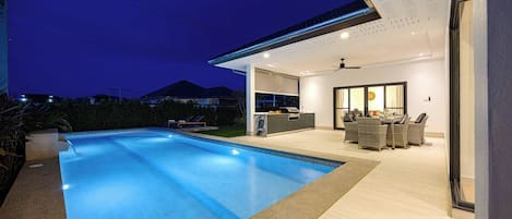 Ein moderner Poolbereich im Freien mit integrierter Küche und Essbereich.