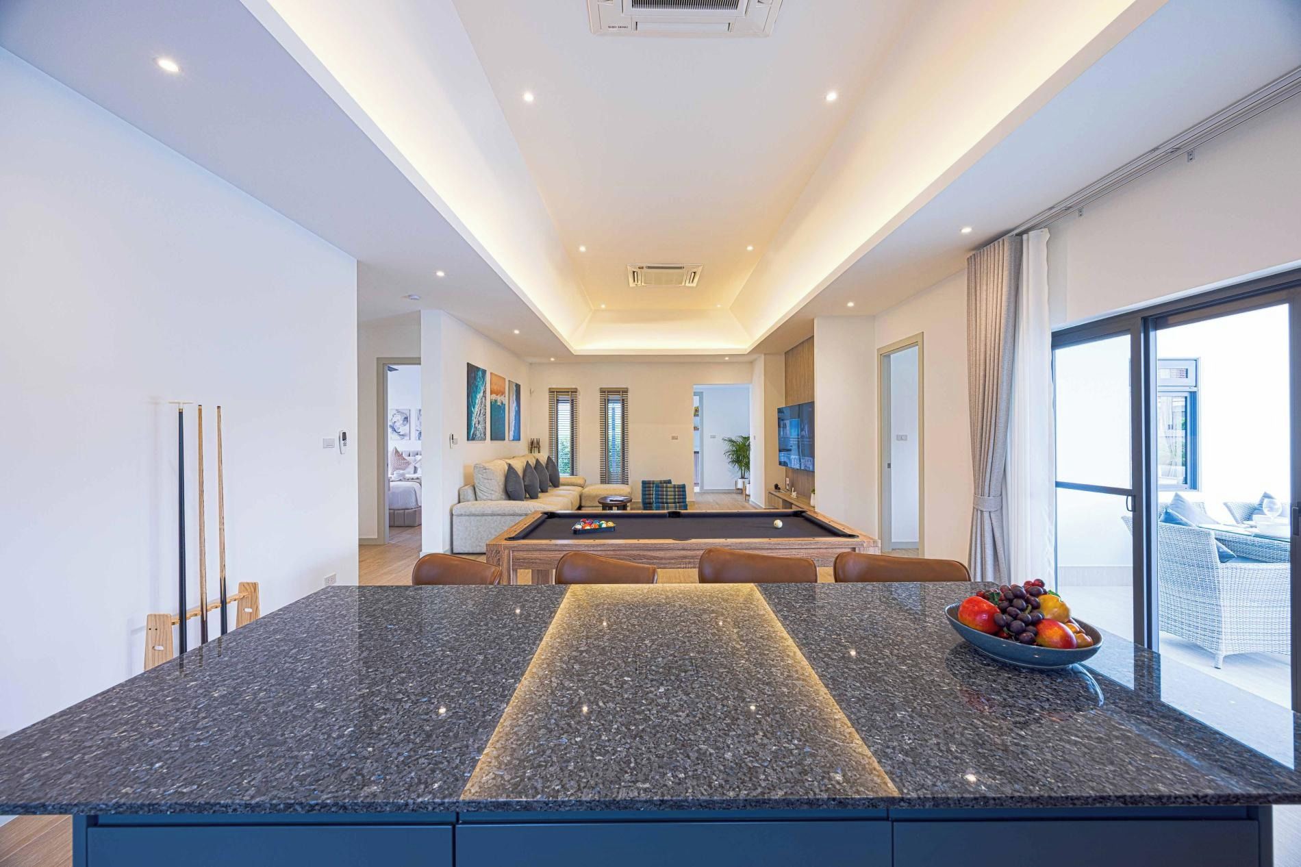 A modern kitchen with a pool table, a dining area, and a large window.