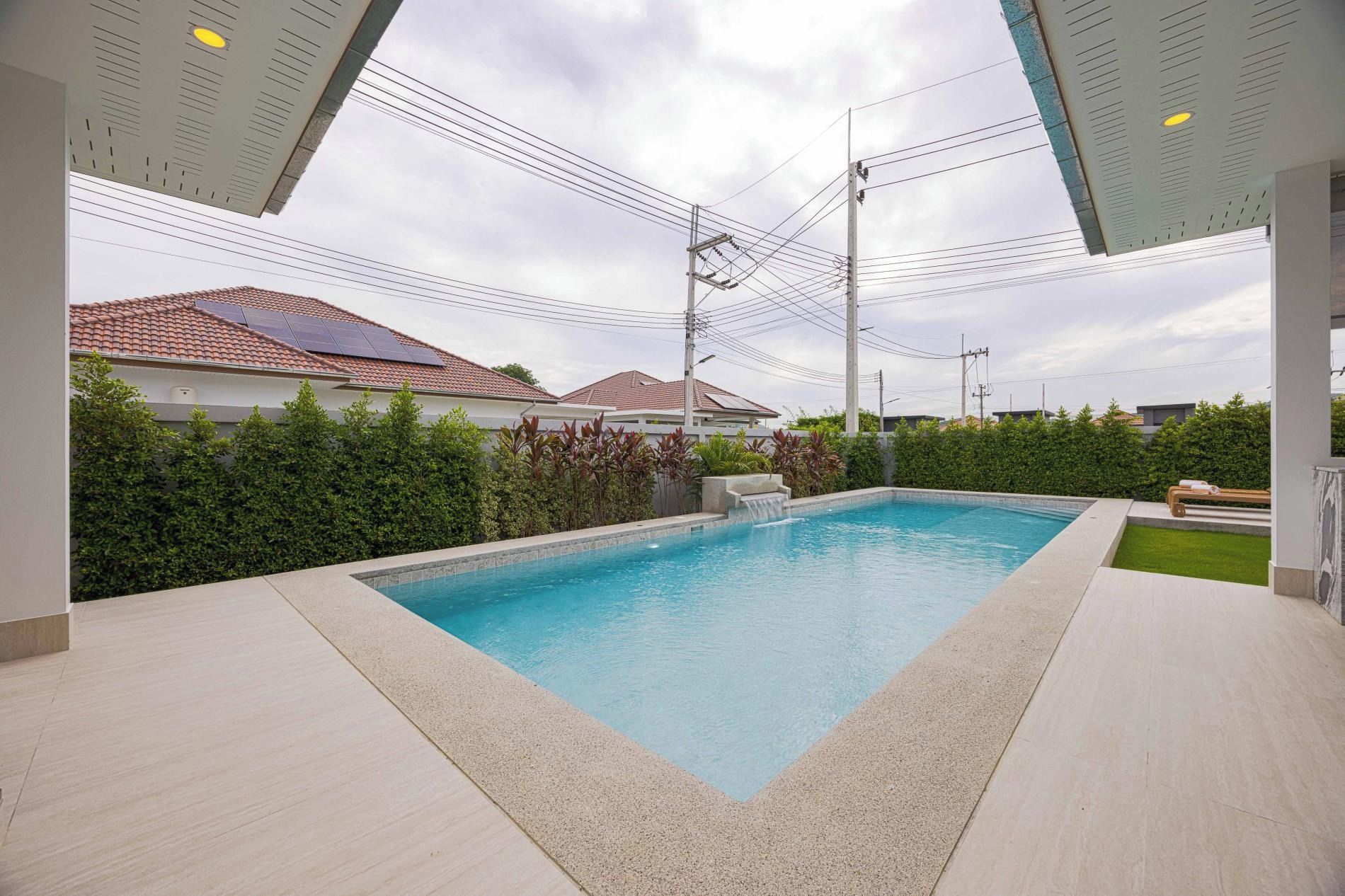 A swimming pool with a surrounding deck, a water feature, and a view of residential buildings with solar panels.