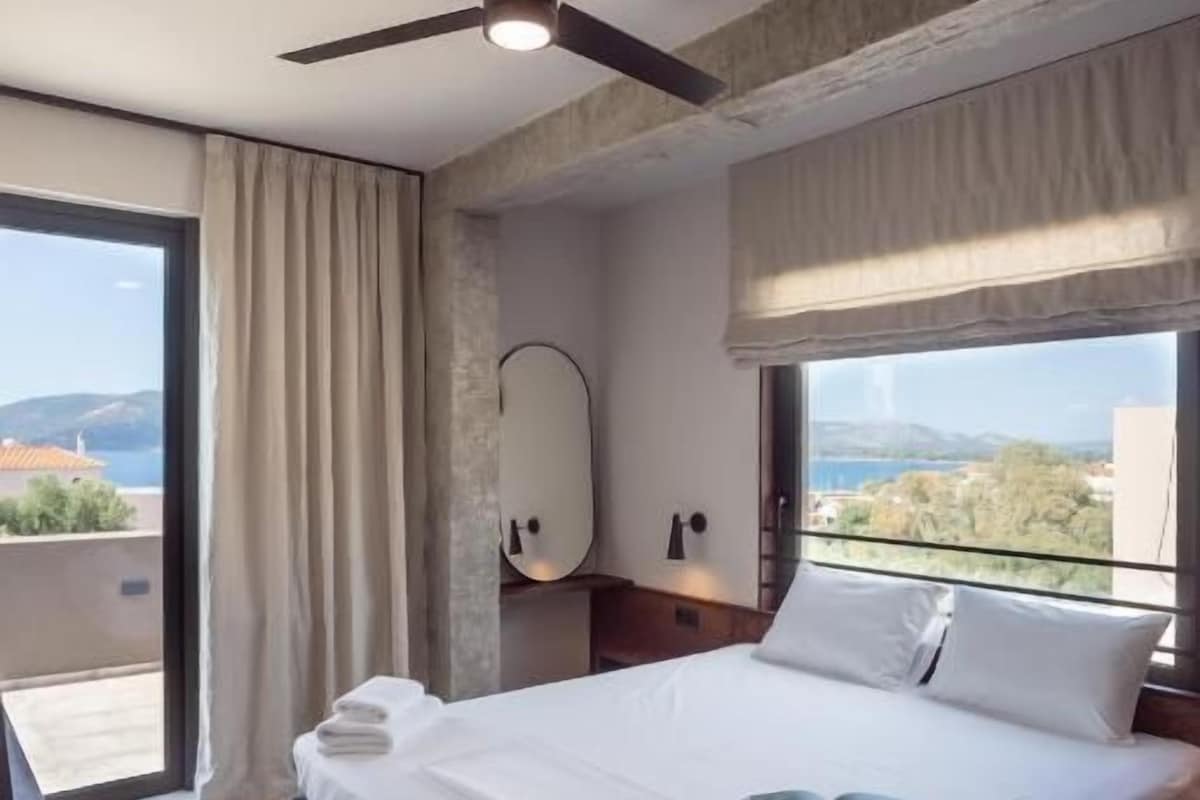 A modern hotel room with a large bed, a ceiling fan, a view of the city, and a balcony.