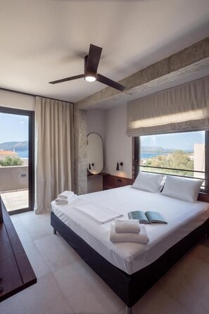 A modern hotel room with a large bed, a ceiling fan, a view of the city, and a balcony.