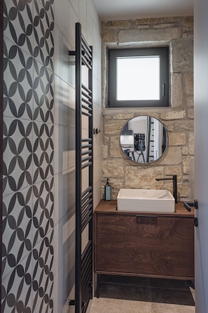 A bathroom with a stone wall, a round mirror, a white sink, and a towel rack.