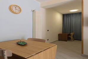 A room with a wooden dining table, chairs, a clock on the wall, a radiator, and a window with curtains. - Casa Musy . (Isola Sacra)