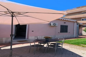 An outdoor seating area with a table and chairs under a large umbrella, a building entrance, and an air conditioning unit on the wall. - Casa Musy . (Isola Sacra)