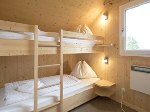 Une chambre avec un lit superposé, une fenêtre, un radiateur fixé au mur et une table de chevet.