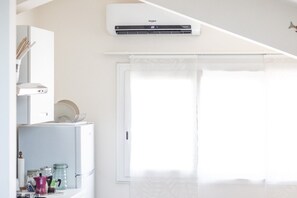 Eine moderne Küche mit integrierter Klimaanlage, einem weißen Kühlschrank und einem Fenster mit weißem Rollo.